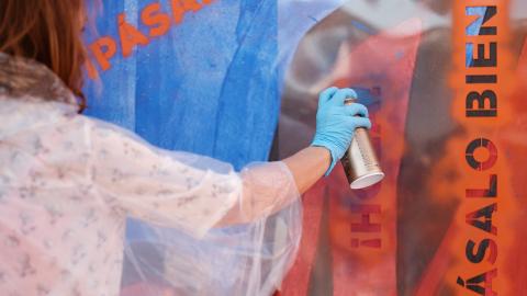 Eine Frau sprüht mit einer Spraydose blaue Farbe an die Team-Aktionswand.