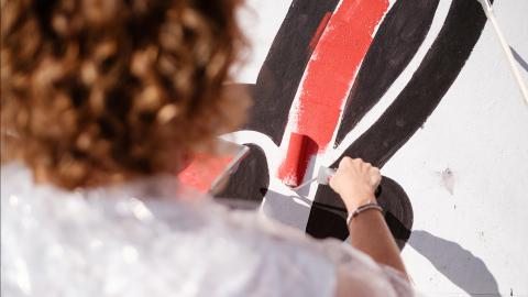 Eine Frau rollt während einer Teambildung mit einer Malerrolle rote Farbe auf einen weißen Hintergrund.