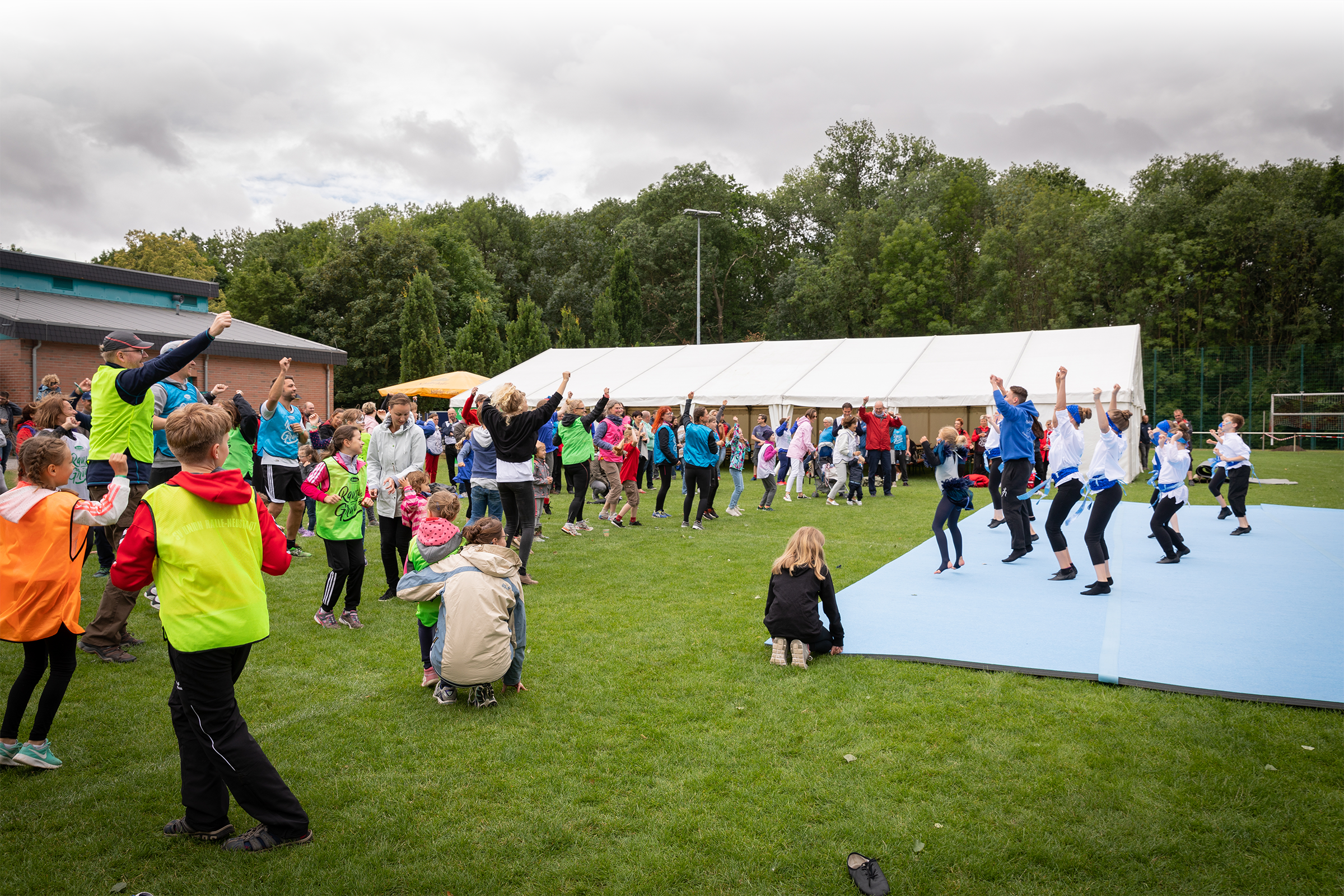 Fest-Wiese mit einer Bühne, auf der Kinder und Jugendliche mit einer Tanz-Performance die Teilnehmer der Mitarbeiterveranstaltung zum Mitmachen animieren.