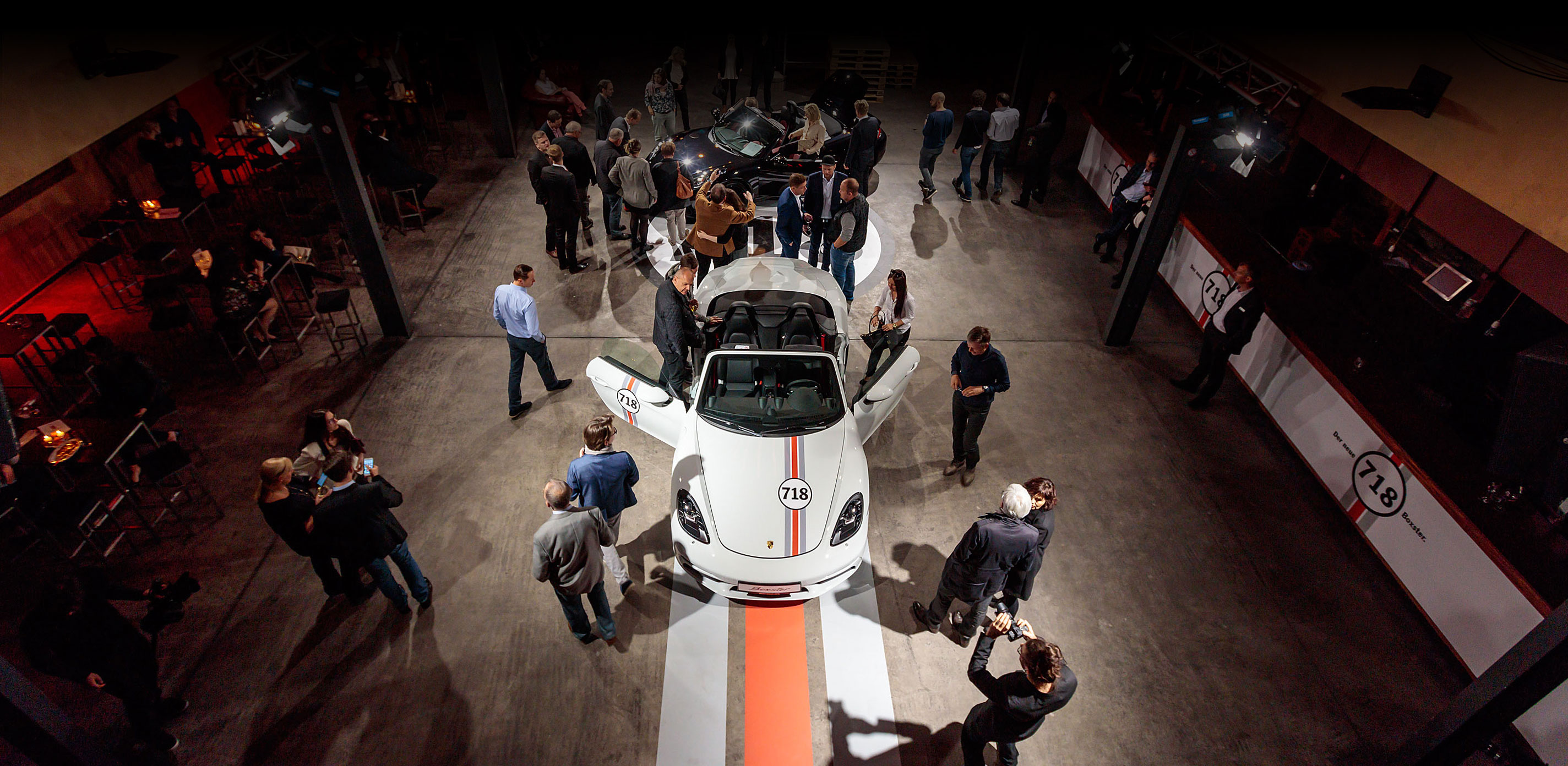 Besucher stehen in der Eventhalle um den neuen Porsche Boxster 718 und schauen ihn sich an.