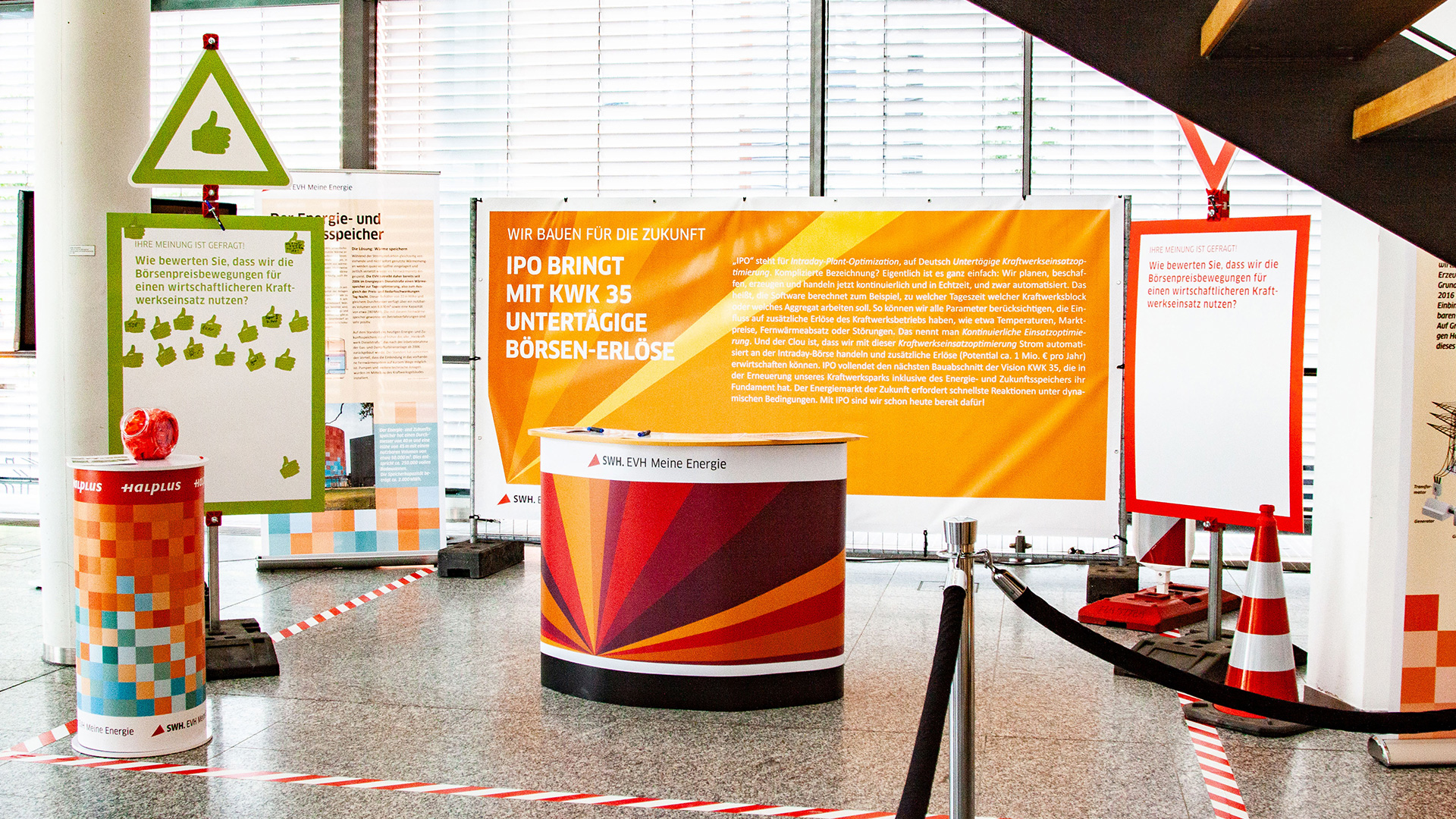 An einem Info-Stand wird der Börsengang (IPO) der SWH vorgestellt. Auf der linken Seite steht eine Tafel im Event-Design mit einigen grünen Daumen-Hoch-Stickern, welche Zustimmung für das vorgestellte Projekt ausdrücken.