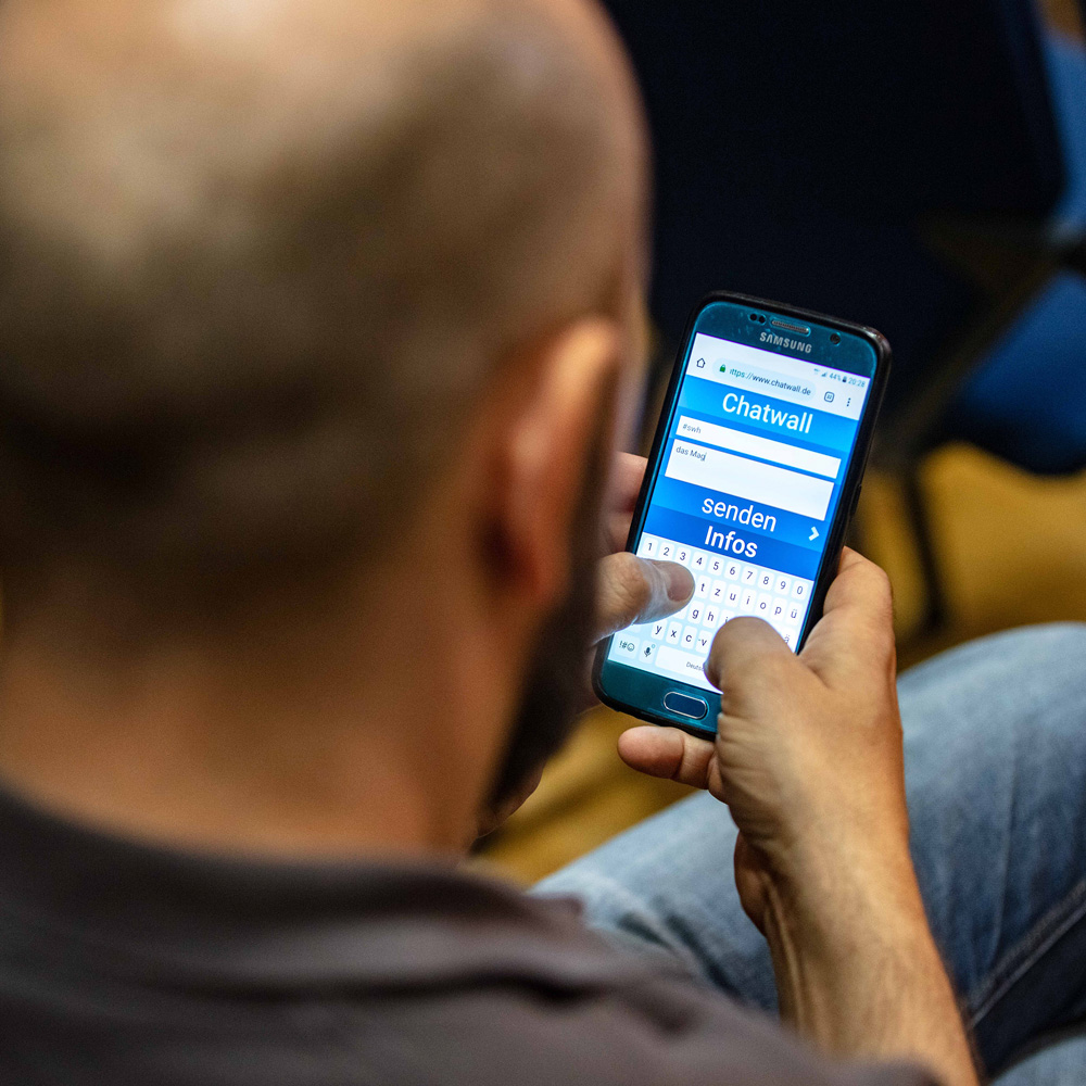 Ein Mitarbeiter nutzt die Umfrage-unktion der EventApp, um sein Feedback über die Chatwall auf der Bühne an die Geschäftsführer zu richten.