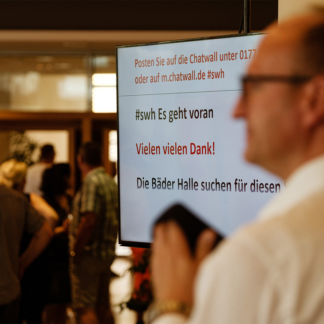 Auf einem Bildschirm wird auf die Nutzung der Chatwall hingewiesen und sich bei den Mitarbeitern für ihre Teilnahme bedankt.