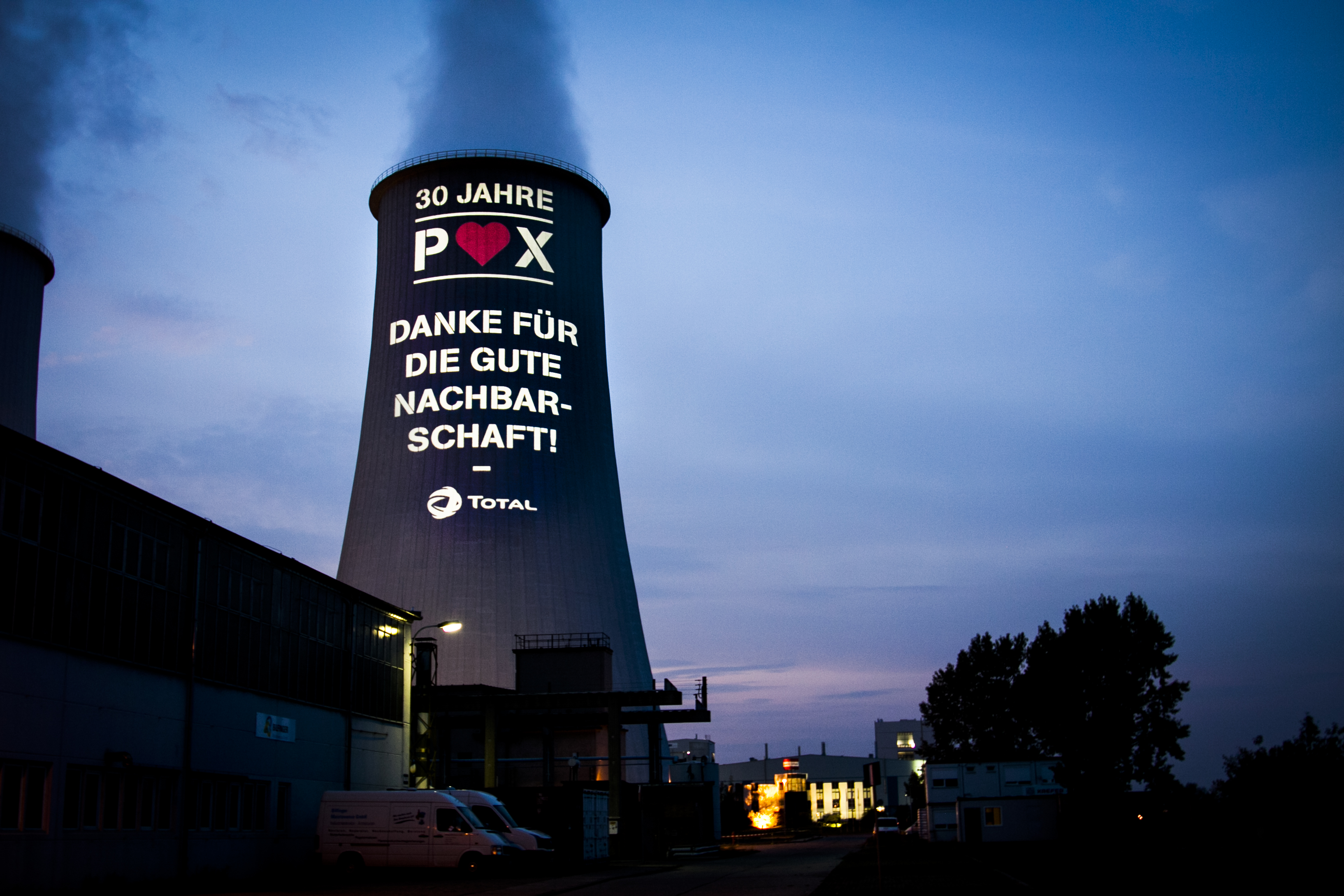 Auf einen Kühlturm der Total Raffinerie Mitteldeutschland GmbH wird eine Pani-Projektion geworfen, um für die gute Beziehung zur Nachbargemeinde zu danken.