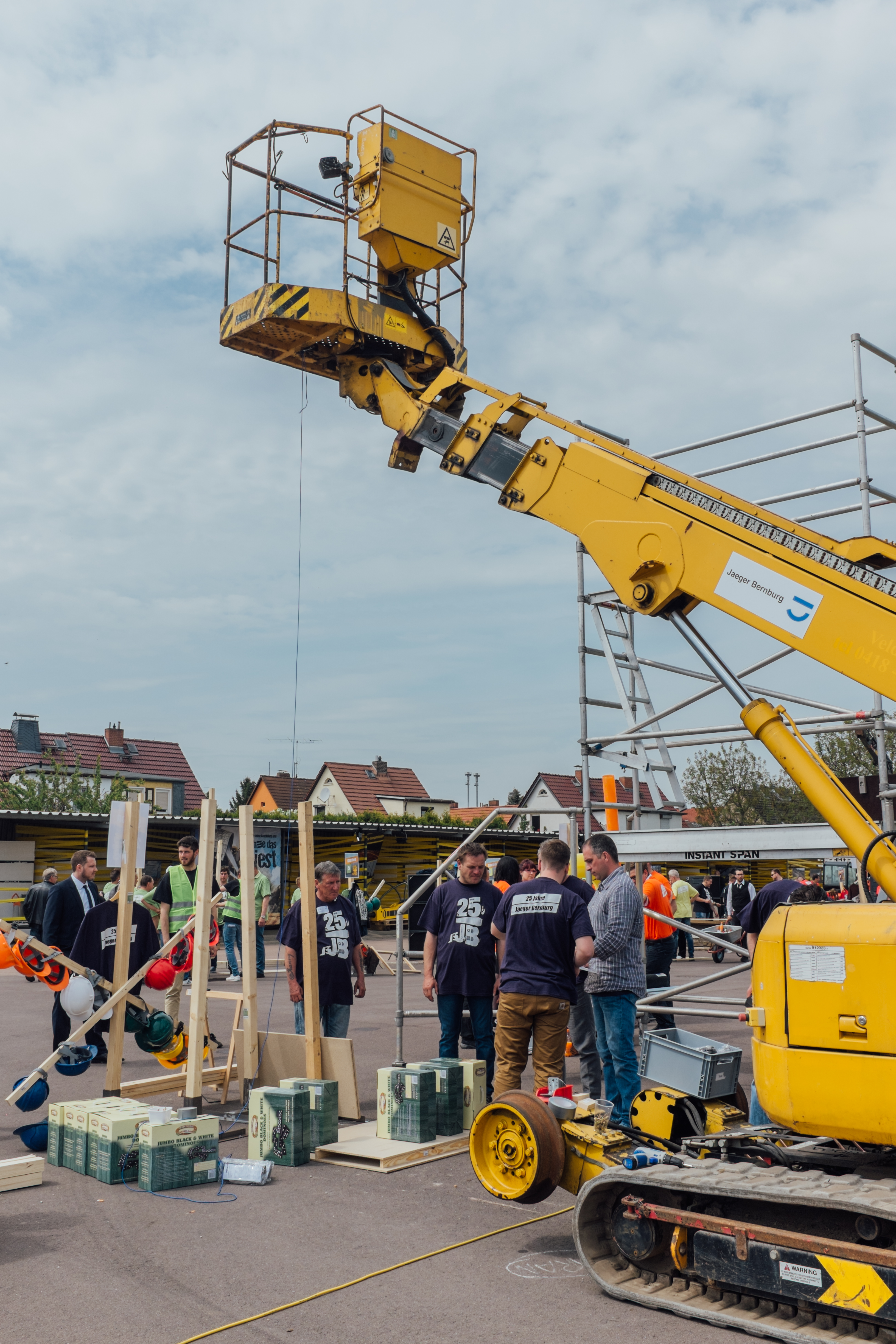 Unter einem Baggerarm stehen Mitarbeiter und bauen an ihrem Projekt mit Holzleisten, welche Teil einer riesigen Kettenreaktion waren.