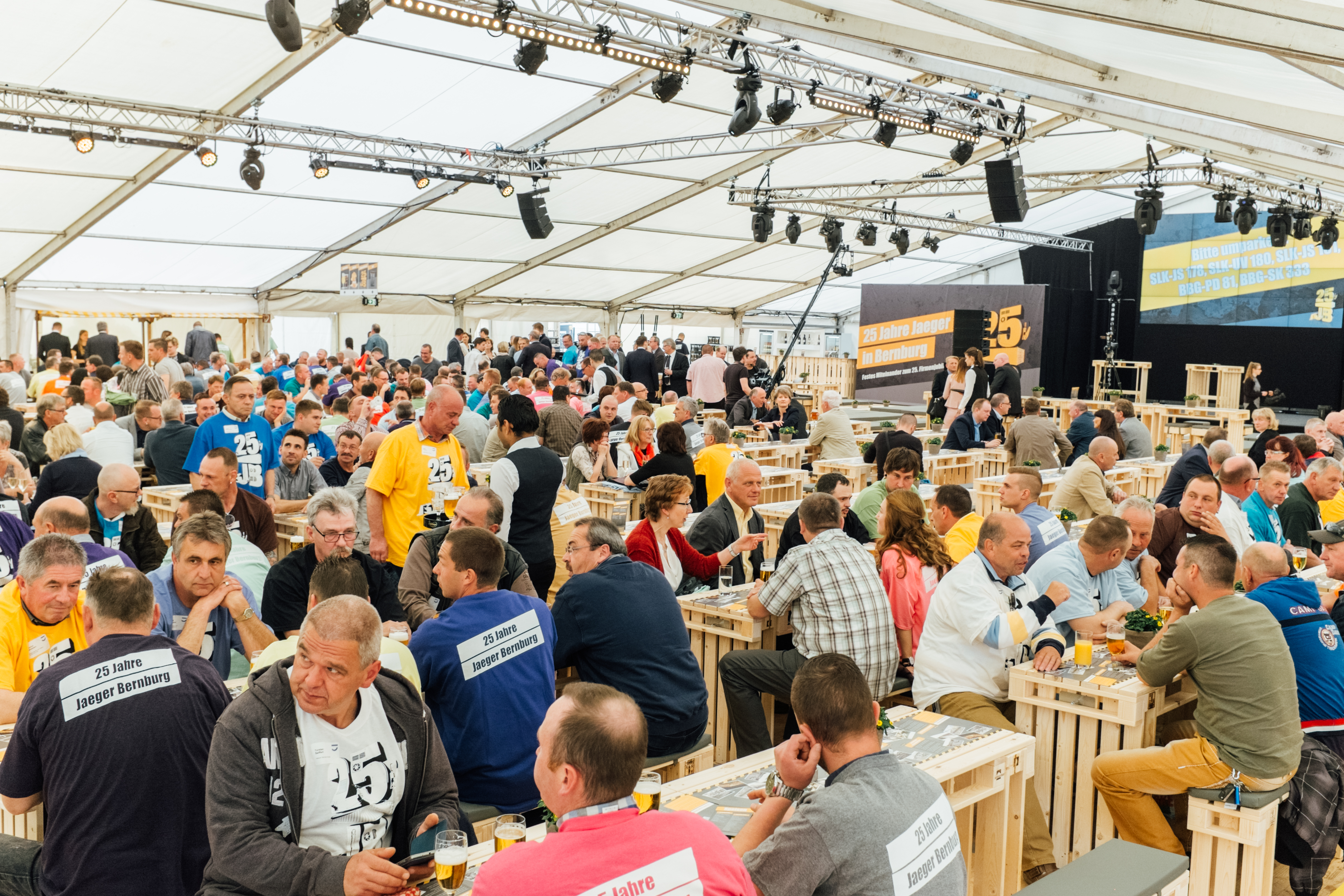 Die Mitarbeiter der Jaeger Bernburg Gruppe sitzen beim Jubiläumsevent an Tischen und tragen ihre Team-T-Shirts.