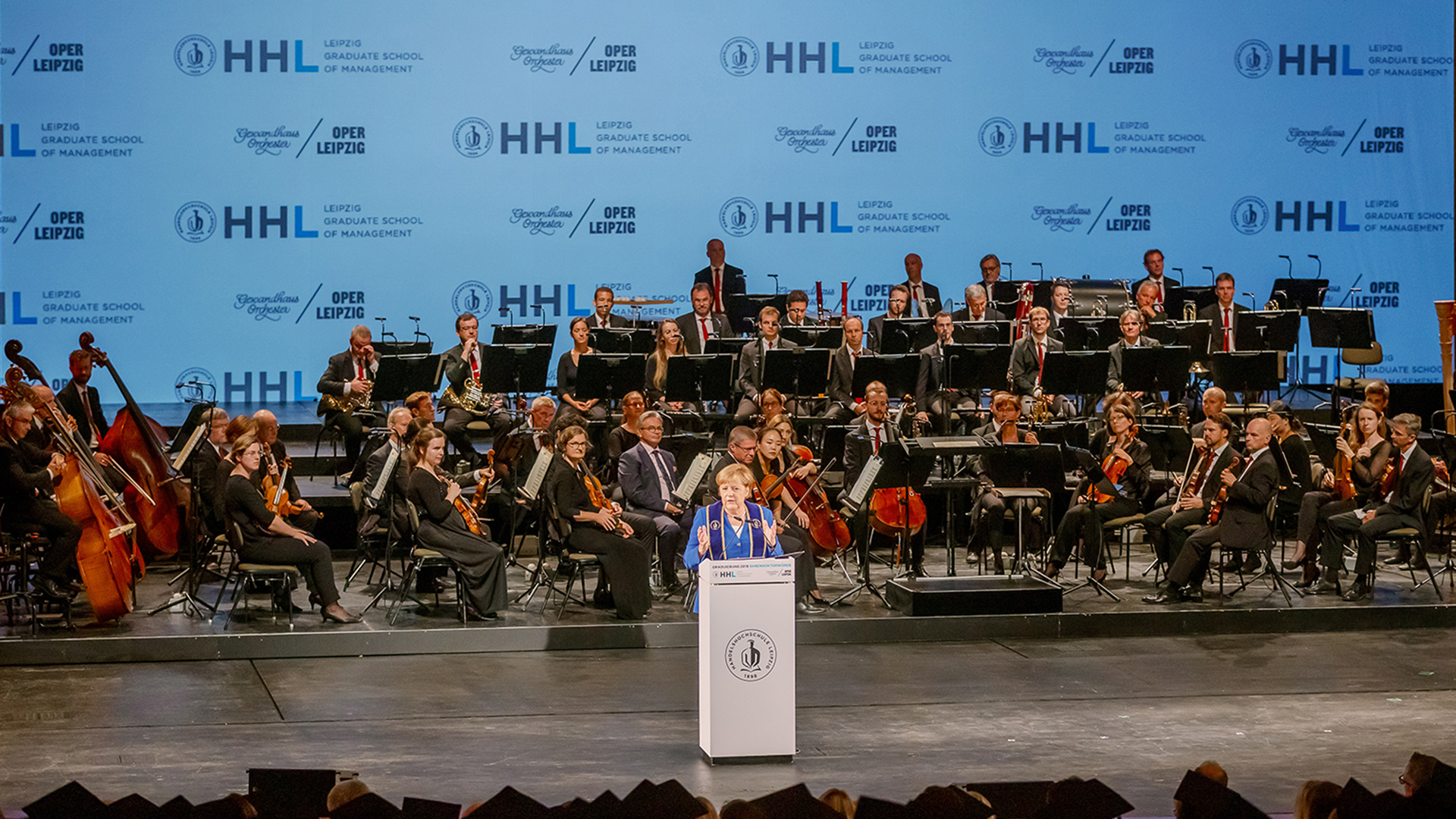 Dr. Angela Merkel hält eine Rede in der Oper Leipzig. Im Hintergrund ist das Gewandhausorchester zu sehen.