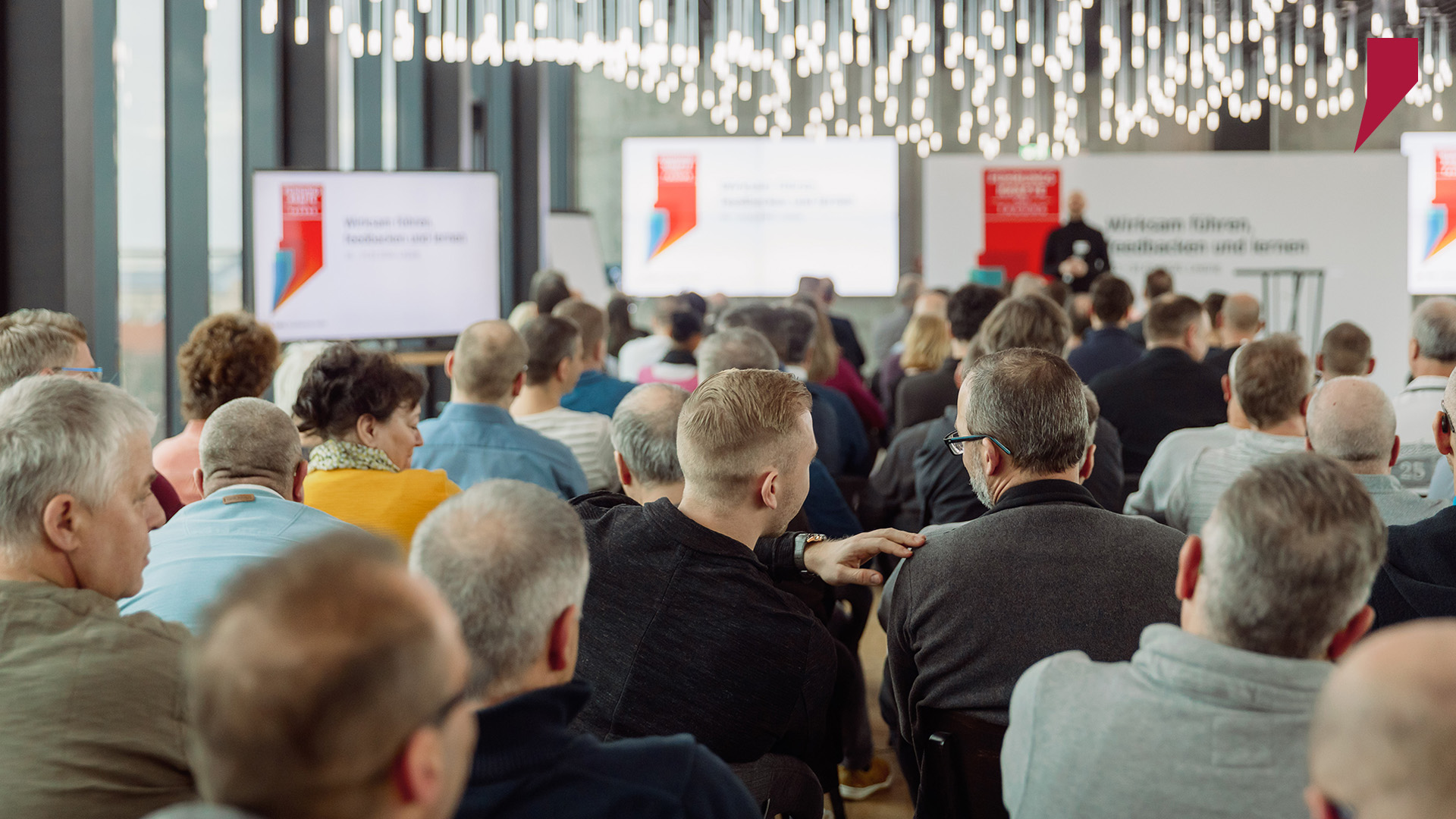 Die operativen Führungskräfte der Stadtwerke Halle verfolgen die Geschehnisse auf der Bühne. Vortragsinhalte werden auf mehreren Bildschirmen multipliziert.